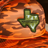 Orange camouflage hunting cap with a green Texas-shaped patch featuring ’Whiskey Myers Hunting Co.’ and duck silhouettes.