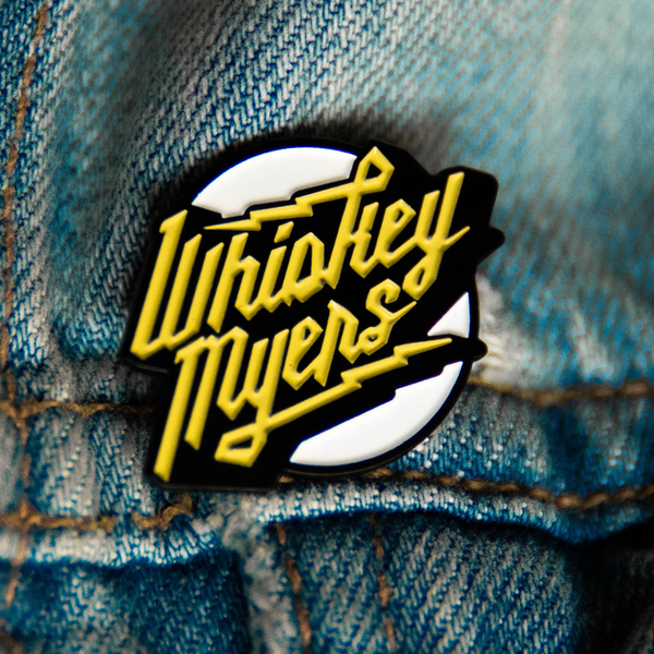 Enamel pin featuring the words ’Whiskey Myers’ in yellow script on a white and black background.